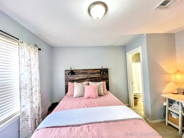 carpeted bedroom featuring multiple windows and ensuite bath