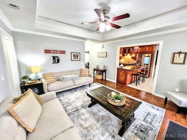 living room featuring ornamental molding, light hardwood / wood-style flooring, ceiling fan, and a tray ceiling