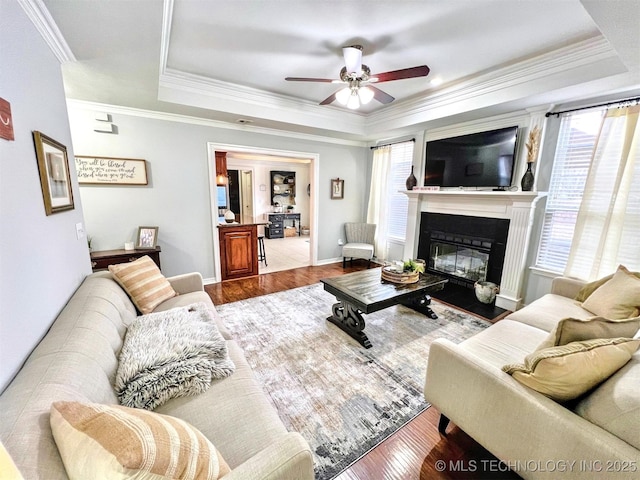 living room featuring wood-type flooring, ornamental molding, and a tray ceiling