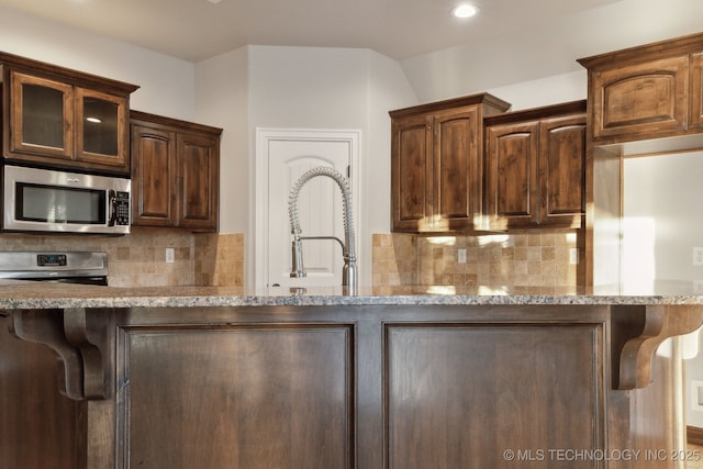 kitchen with stainless steel appliances, tasteful backsplash, dark brown cabinetry, and light stone counters