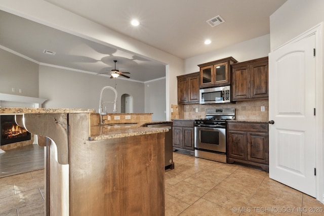 kitchen with sink, stainless steel appliances, light stone counters, ornamental molding, and decorative backsplash