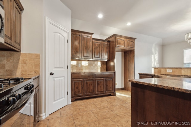 kitchen featuring light tile patterned flooring, decorative backsplash, range with gas cooktop, and dark stone countertops