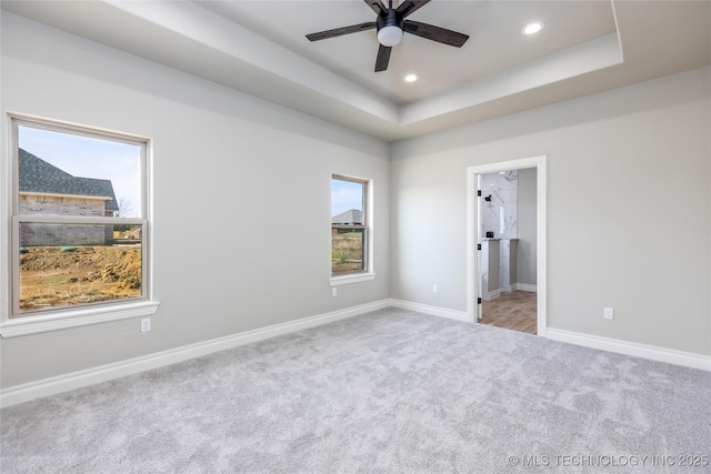 unfurnished bedroom with a raised ceiling, connected bathroom, and light colored carpet