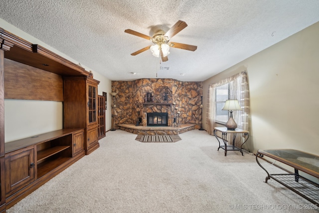 carpeted living room with ceiling fan, a stone fireplace, and a textured ceiling