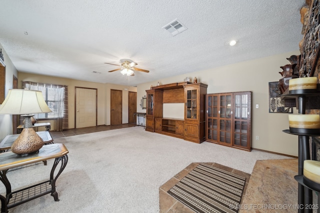 carpeted living room featuring ceiling fan and a textured ceiling