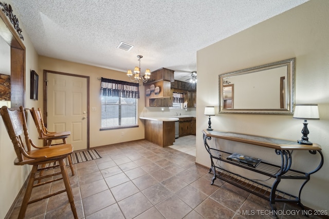 kitchen featuring light tile patterned floors, hanging light fixtures, a textured ceiling, ceiling fan with notable chandelier, and kitchen peninsula