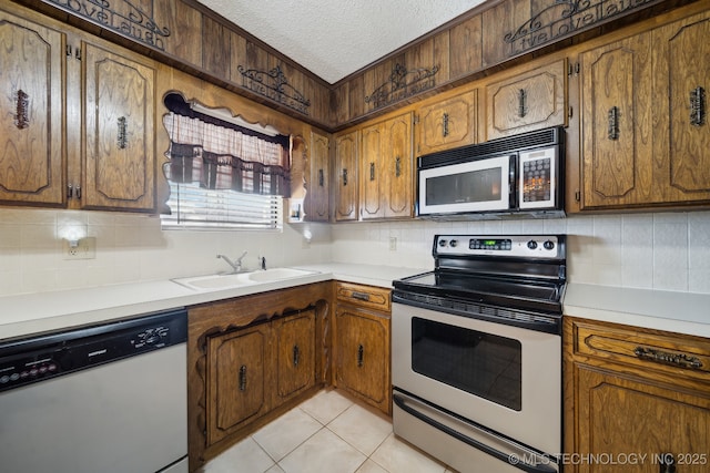 kitchen with sink, backsplash, light tile patterned floors, stainless steel appliances, and a textured ceiling