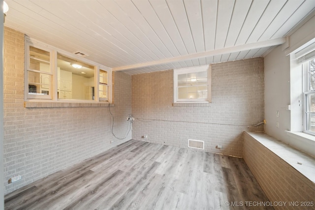 empty room with beam ceiling, wood-type flooring, wooden ceiling, and brick wall