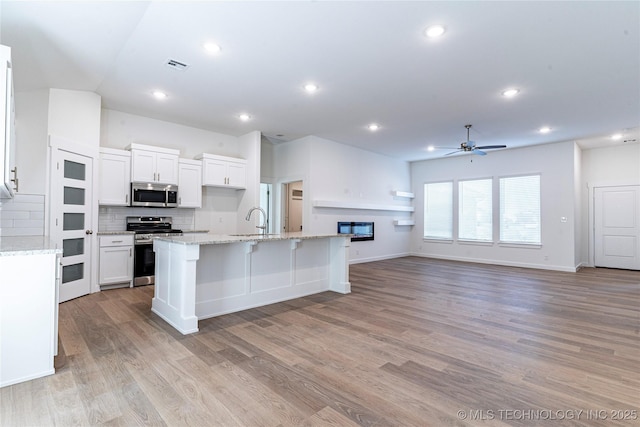 kitchen with appliances with stainless steel finishes, white cabinetry, backsplash, a center island with sink, and light wood-type flooring