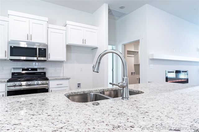 kitchen featuring stainless steel appliances, white cabinetry, sink, and light stone counters