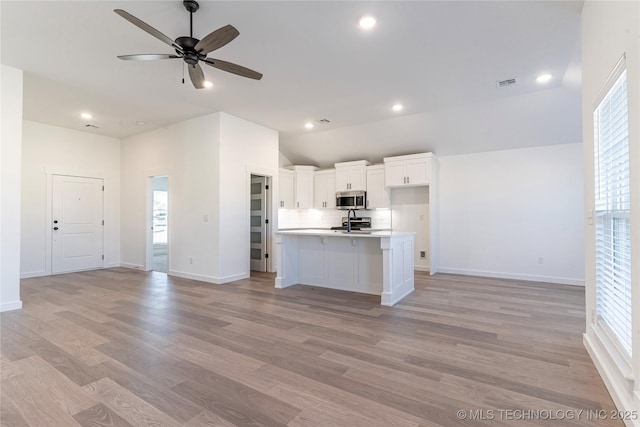 kitchen featuring vaulted ceiling, white cabinets, ceiling fan, a center island with sink, and light wood-type flooring