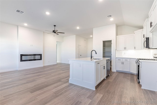 kitchen with appliances with stainless steel finishes, sink, white cabinets, light hardwood / wood-style floors, and a center island with sink