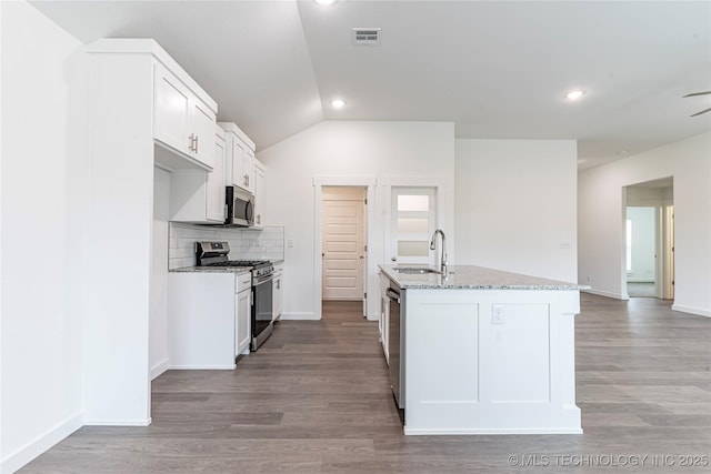 kitchen with appliances with stainless steel finishes, an island with sink, sink, white cabinets, and light stone counters