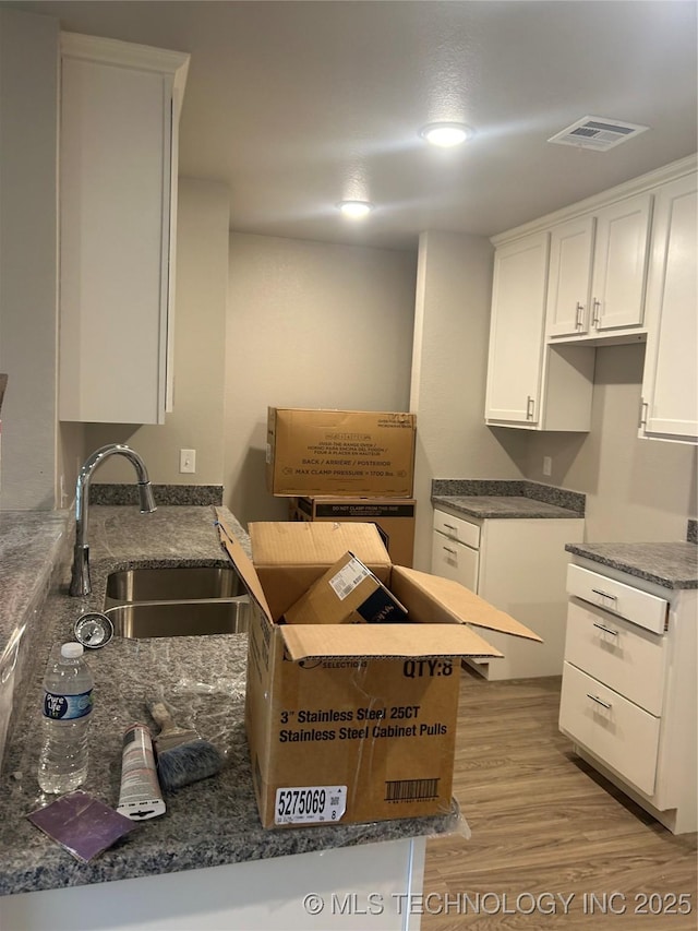 kitchen featuring sink, dark stone countertops, white cabinets, and light hardwood / wood-style floors