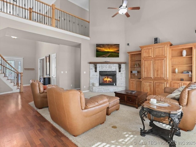 living room with a high ceiling, wood-type flooring, ceiling fan, and a fireplace