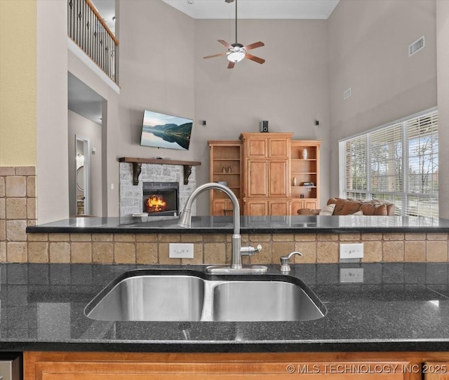 kitchen featuring ceiling fan, a towering ceiling, a fireplace, and sink