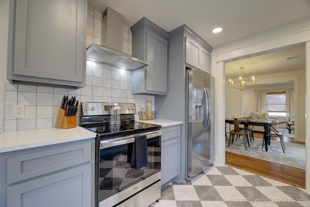 kitchen featuring appliances with stainless steel finishes, wall chimney exhaust hood, decorative backsplash, and a notable chandelier