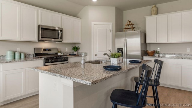 kitchen with white cabinetry, appliances with stainless steel finishes, sink, and a center island with sink