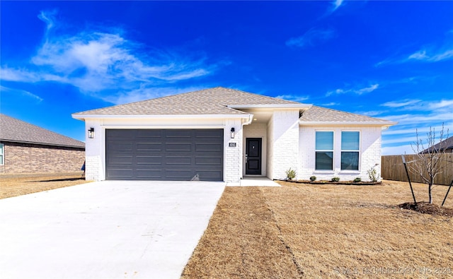 view of front of property featuring concrete driveway, roof with shingles, an attached garage, fence, and brick siding