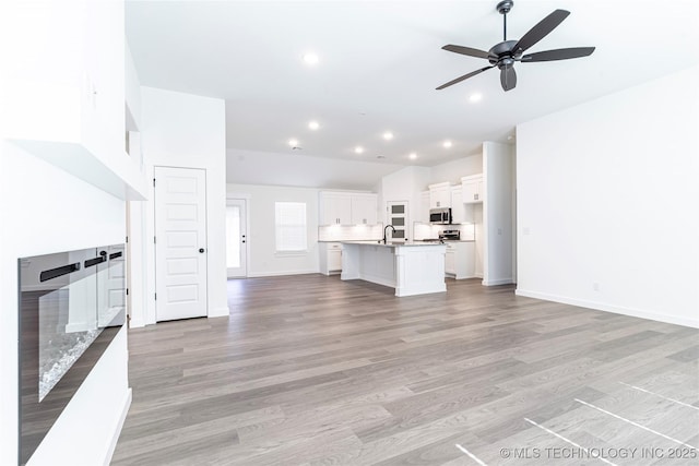 unfurnished living room featuring baseboards, a ceiling fan, light wood-style flooring, and recessed lighting