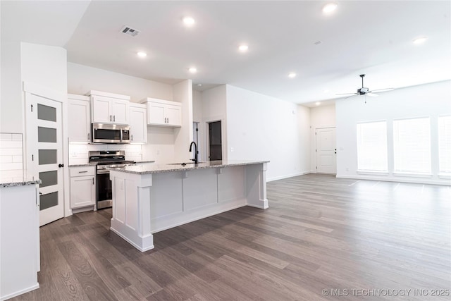 kitchen featuring white cabinetry, appliances with stainless steel finishes, decorative backsplash, dark wood-style floors, and a center island with sink