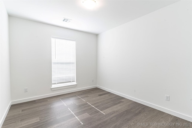 spare room with dark wood-type flooring, visible vents, and baseboards