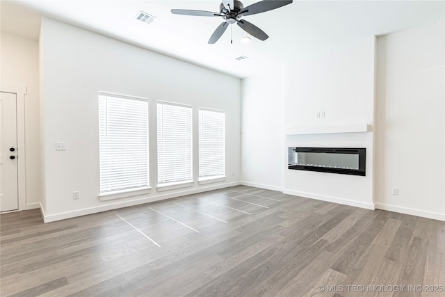 unfurnished living room featuring baseboards, visible vents, a glass covered fireplace, ceiling fan, and wood finished floors