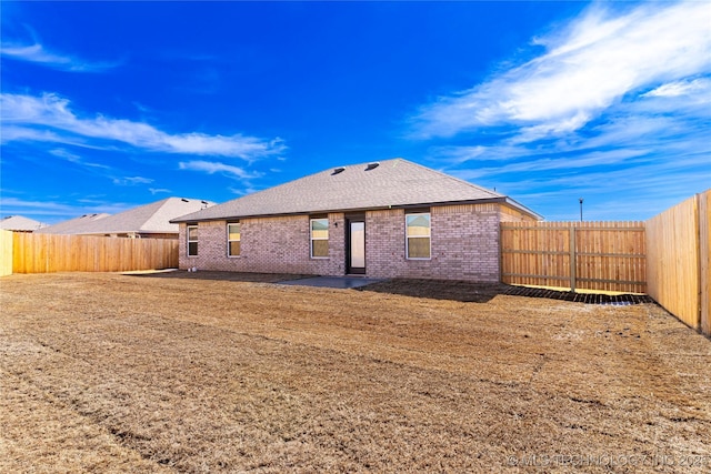 back of house featuring a fenced backyard, roof with shingles, and brick siding