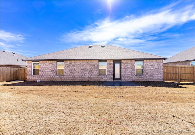 back of property featuring brick siding, roof with shingles, and a fenced backyard