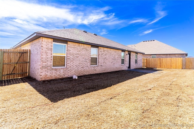 back of property featuring a shingled roof, a fenced backyard, and brick siding