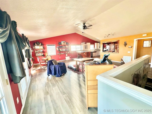 living room featuring rail lighting, ceiling fan, wood-type flooring, a textured ceiling, and vaulted ceiling