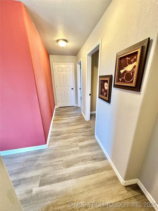 corridor with a textured ceiling and light wood-type flooring