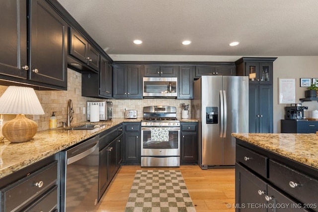 kitchen featuring tasteful backsplash, sink, stainless steel appliances, light stone countertops, and light hardwood / wood-style flooring