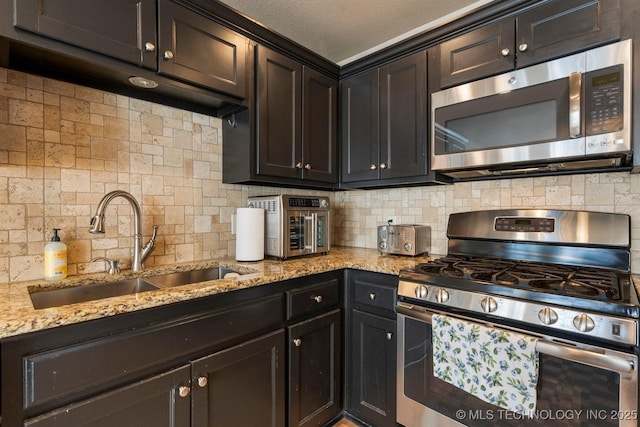 kitchen featuring sink, backsplash, light stone countertops, and appliances with stainless steel finishes