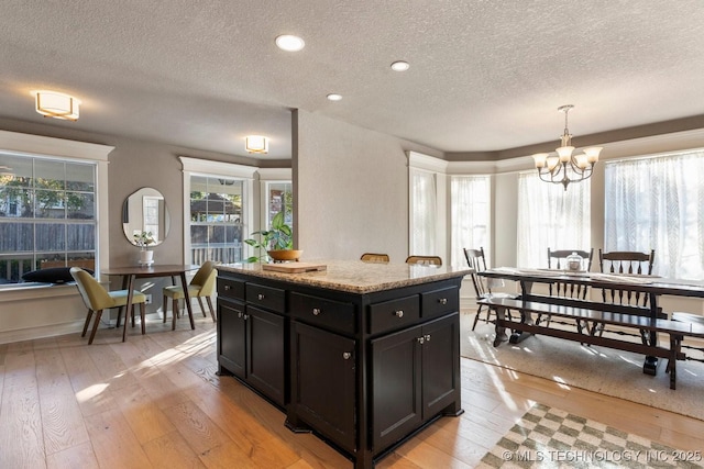 kitchen with a kitchen island, decorative light fixtures, a chandelier, light stone countertops, and light hardwood / wood-style flooring