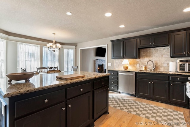 kitchen featuring sink, light stone countertops, a kitchen island, stainless steel dishwasher, and light wood-type flooring