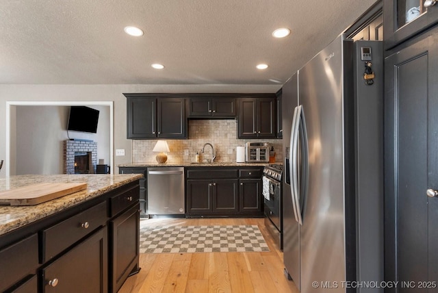 kitchen featuring sink, backsplash, light stone counters, stainless steel appliances, and light wood-type flooring