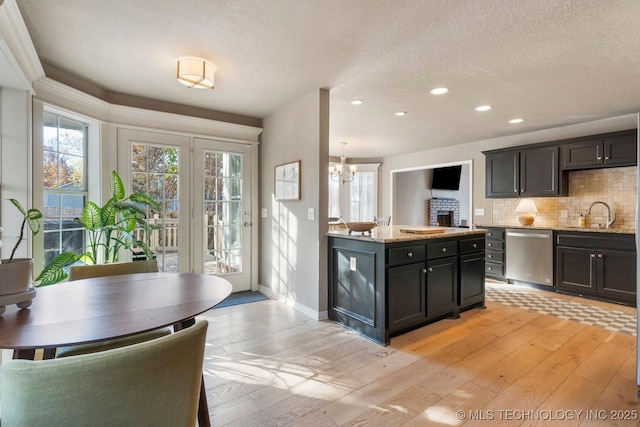 kitchen with light stone counters, tasteful backsplash, light wood-type flooring, dishwasher, and pendant lighting