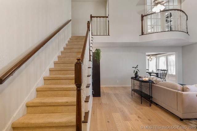 stairway with hardwood / wood-style flooring, ceiling fan with notable chandelier, and a high ceiling