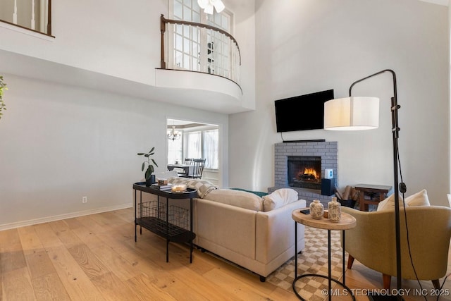 living room featuring an inviting chandelier, a brick fireplace, a towering ceiling, and light wood-type flooring