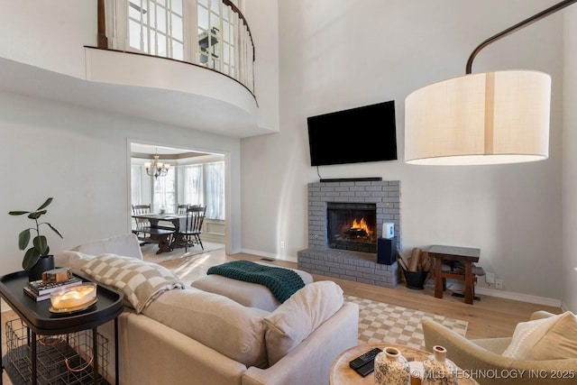 living room with hardwood / wood-style flooring, a notable chandelier, a brick fireplace, and a high ceiling