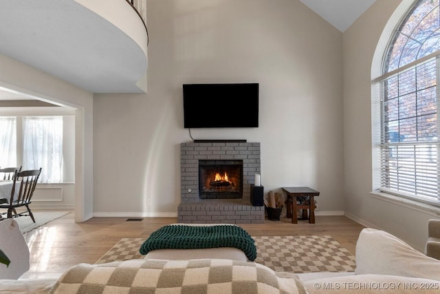 living room with a brick fireplace, high vaulted ceiling, and light hardwood / wood-style floors