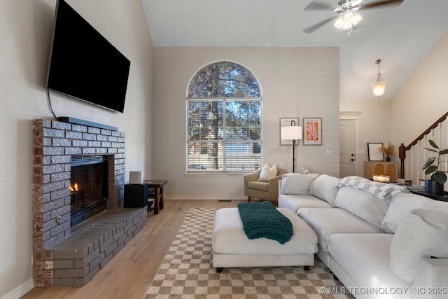 living room with ceiling fan, a fireplace, vaulted ceiling, and light wood-type flooring