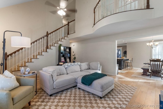 living room featuring ceiling fan with notable chandelier, a high ceiling, and light wood-type flooring