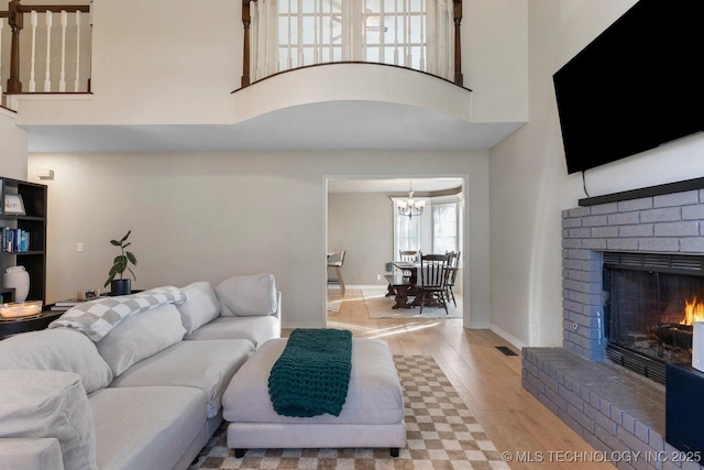 living room featuring an inviting chandelier, a fireplace, light hardwood / wood-style flooring, and a high ceiling