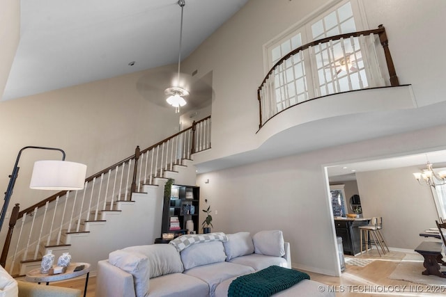 living room featuring ceiling fan with notable chandelier, light wood-type flooring, and a high ceiling