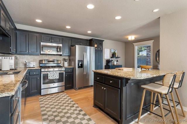 kitchen featuring appliances with stainless steel finishes, light stone counters, tasteful backsplash, a kitchen bar, and light wood-type flooring