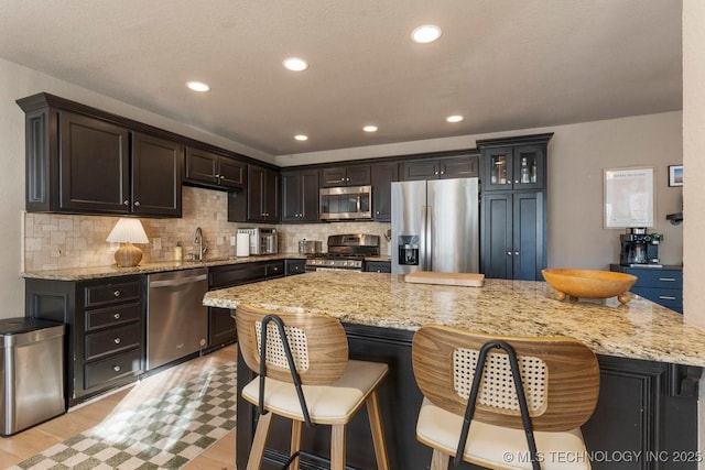 kitchen with stainless steel appliances, tasteful backsplash, a center island, and light stone counters