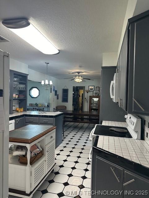 kitchen featuring tile counters, kitchen peninsula, white appliances, and decorative light fixtures