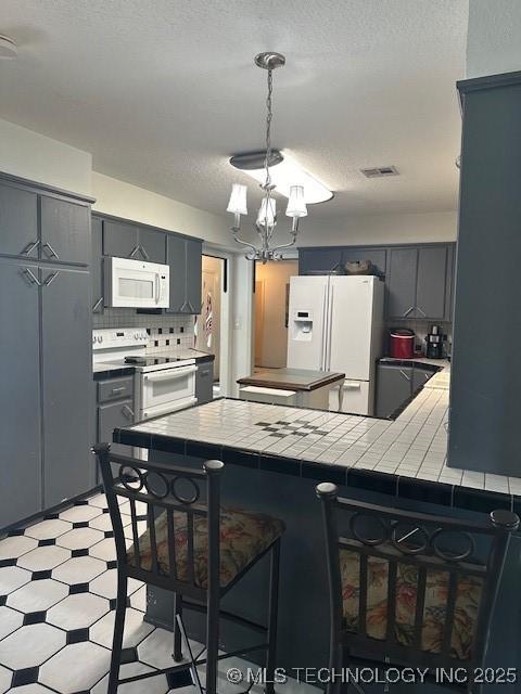 kitchen with white appliances, a textured ceiling, decorative backsplash, tile countertops, and kitchen peninsula